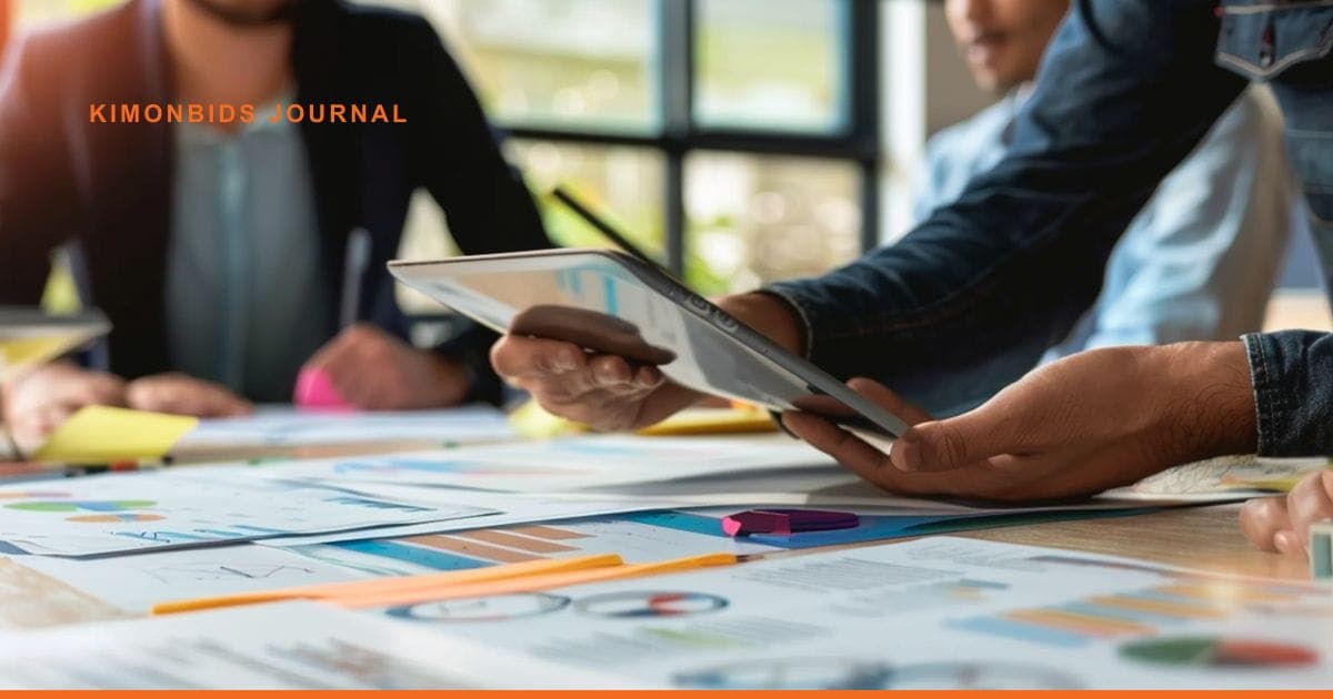 A team passes a tablet across a table covered in printed charts, graphs and sticky notes.